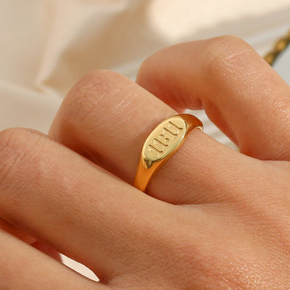 Gold angel number ring with engraved text on a person's finger against a neutral background